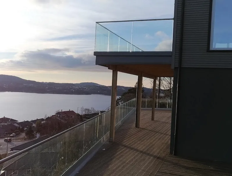 Helglassrekkverk på balkong på hus med utsikt over havenby i solnedgang